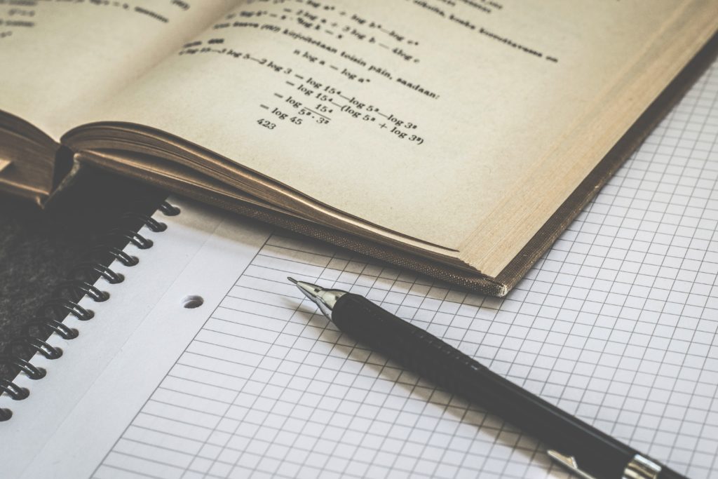 Image of book open on top of a graph paper notebook, with a pen.